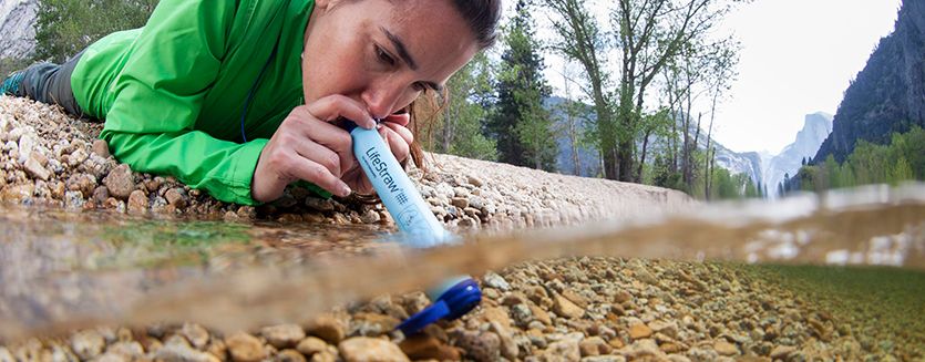 Vrouw gebruikt een LifeStraw waterfilter in een rivier